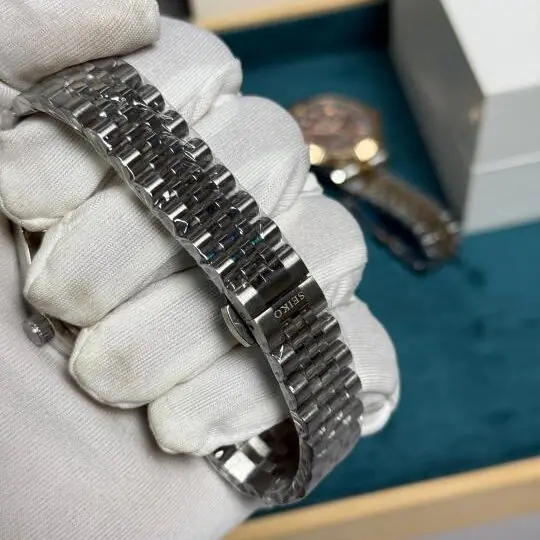 Se1ko green sunburst dial watch with fluted bezel and silver jubilee bracelet displayed on white gloved hand in watch box