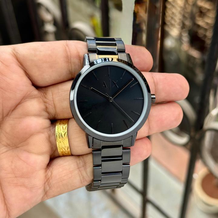 A|X Arm4ni Exch4nge full black minimalist watch with AX logo dial, gold-tone hands, and black PVD stainless steel bracelet held on velvet cushion